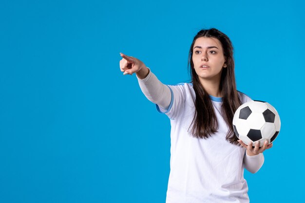 Vista frontal de las mujeres jóvenes con balón de fútbol en la pared azul