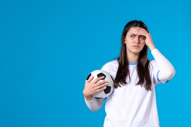 Vista frontal de las mujeres jóvenes con balón de fútbol en la pared azul