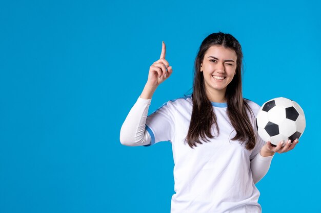 Vista frontal de las mujeres jóvenes con balón de fútbol en la pared azul