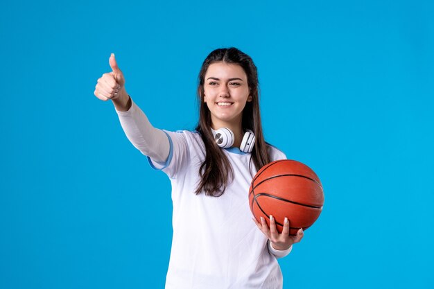 Vista frontal de las mujeres jóvenes con baloncesto en la pared azul