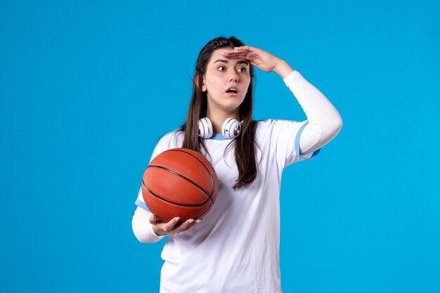 Vista frontal de las mujeres jóvenes con baloncesto en la pared azul