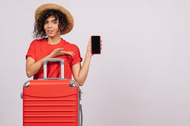 Vista frontal de las mujeres jóvenes con bolsa preparándose para el viaje sosteniendo el teléfono sobre un fondo blanco, viaje de sol, avión, vacaciones turísticas, vuelo de descanso de color