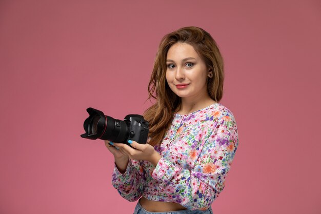 Vista frontal de las mujeres jóvenes en camisa de diseño floral y jeans sosteniendo una cámara de fotos en el fondo rosa