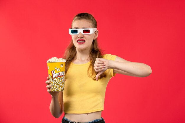 Vista frontal de las mujeres jóvenes en el cine con paquete de palomitas de maíz en -d gafas de sol en la pared roja películas cine cine