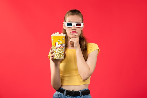 Foto gratuita vista frontal de las mujeres jóvenes en el cine sosteniendo palomitas de maíz en -d gafas de sol y pensando en la pared roja cine cine snack película divertida