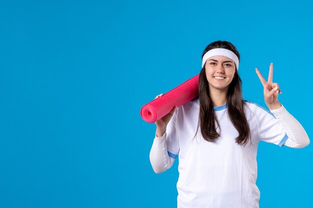 Vista frontal de las mujeres jóvenes con estera de yoga en la pared azul