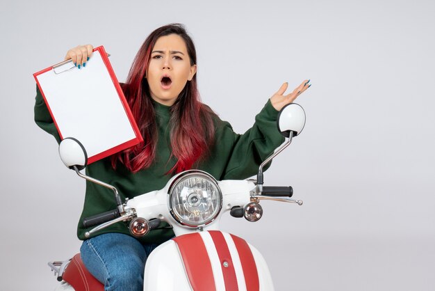 Vista frontal de las mujeres jóvenes en motocicleta sosteniendo una nota para la firma en la pared blanca