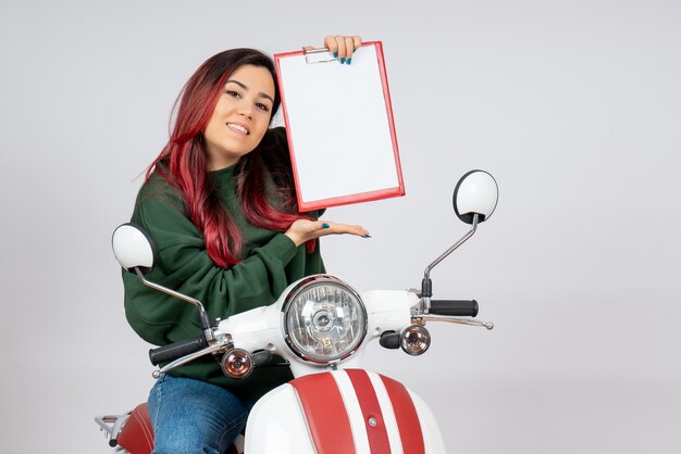 Vista frontal de las mujeres jóvenes en motocicleta sosteniendo una nota para la firma en la pared blanca