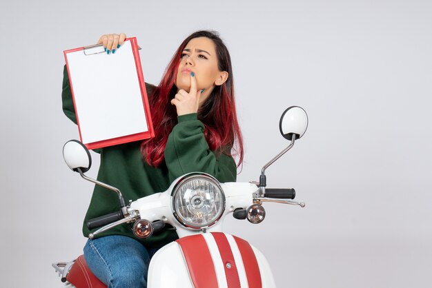 Vista frontal de las mujeres jóvenes en motocicleta sosteniendo una nota para la firma en la pared blanca