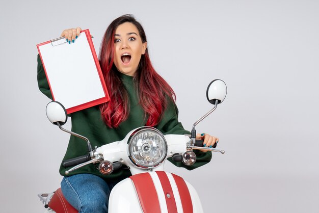 Vista frontal de las mujeres jóvenes en motocicleta sosteniendo una nota para la firma en la pared blanca