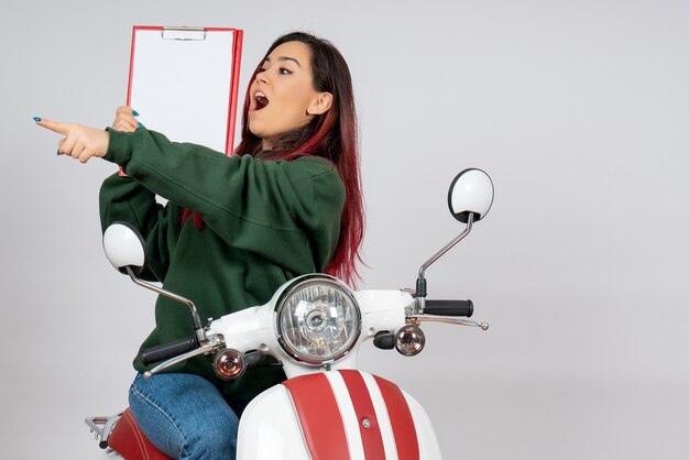 Vista frontal de las mujeres jóvenes en motocicleta sosteniendo una nota para la firma en la pared blanca