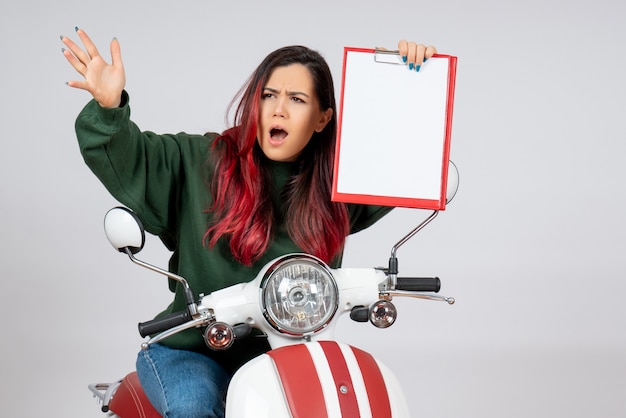 Vista frontal de las mujeres jóvenes en motocicleta sosteniendo una nota para la firma en la pared blanca