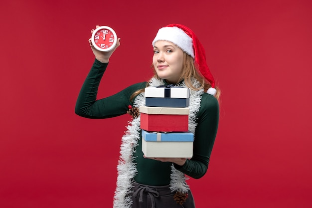 Foto gratuita vista frontal de las mujeres jóvenes con regalos y reloj sobre fondo rojo.