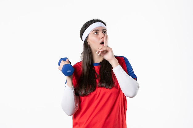 Vista frontal de las mujeres jóvenes en ropa deportiva trabajando con pesas en la pared blanca