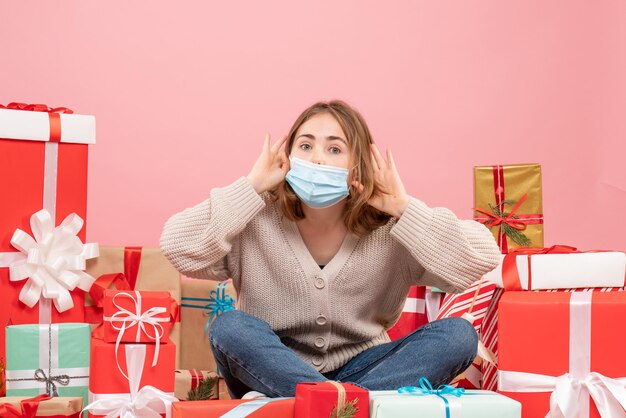 Vista frontal de las mujeres jóvenes sentados alrededor de regalos de Navidad en máscara