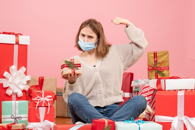 Vista frontal de las mujeres jóvenes sentados alrededor de regalos de Navidad en máscara