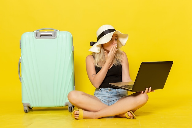 Vista frontal de las mujeres jóvenes usando su computadora portátil en la pared amarilla viaje vacaciones viaje femenino viaje sol