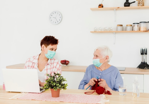 Vista frontal de las mujeres mayores que usan máscaras médicas en casa mientras realizan actividades