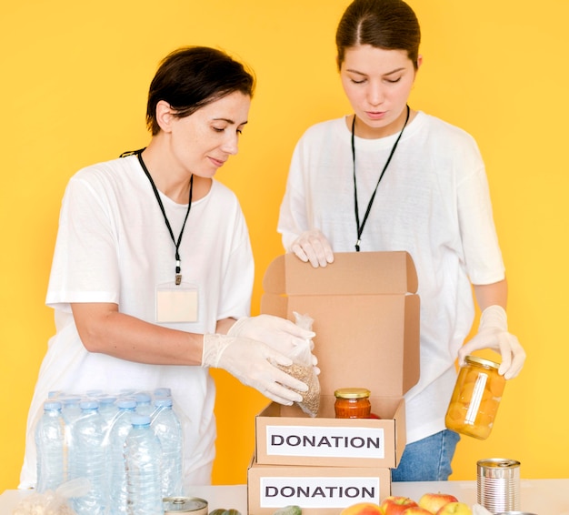 Vista frontal de mujeres poniendo comida en caja de donación