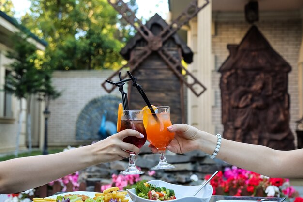 Vista frontal mujeres tintinean vasos con refrescantes cócteles al aire libre