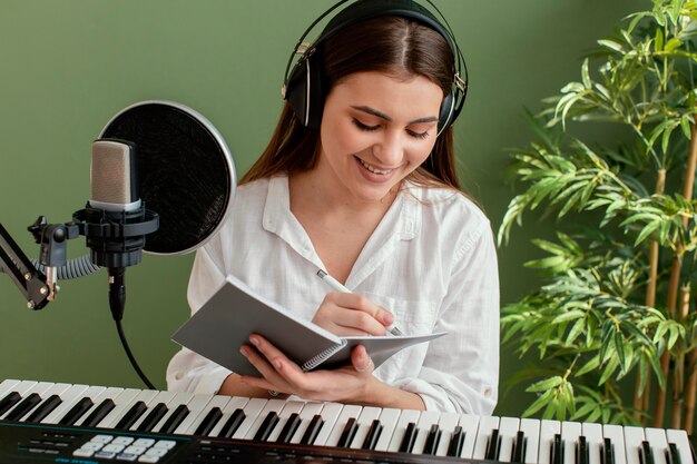 Vista frontal del músico femenino sonriente tocando el teclado del piano y escribiendo canciones durante la grabación