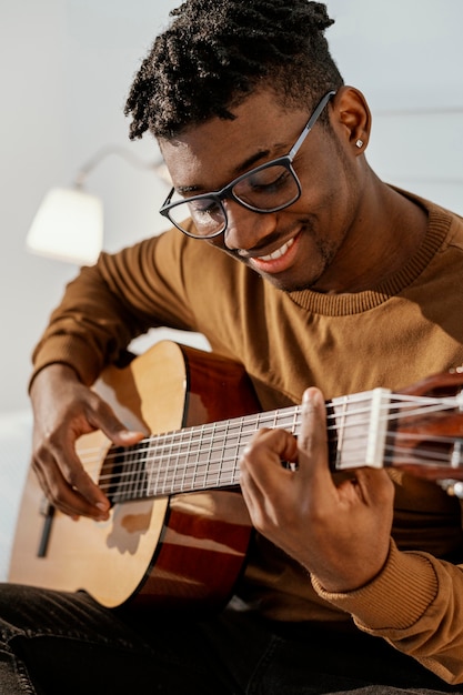 Vista frontal del músico masculino sonriente en casa tocando la guitarra en la cama
