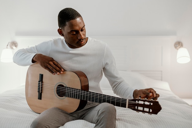 Vista frontal del músico masculino tocando la guitarra en la cama