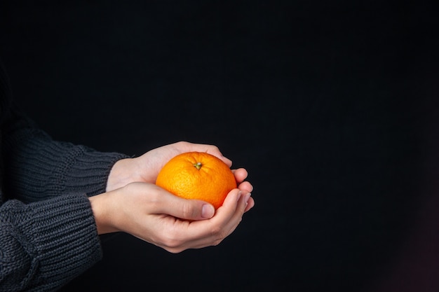 Vista frontal de naranja fresca en manos masculinas en la oscuridad