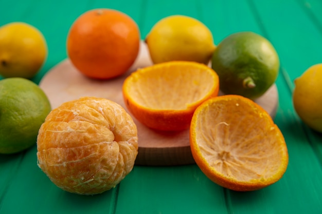 Foto gratuita vista frontal de naranja pelada con cáscaras y limones con limas sobre un fondo verde