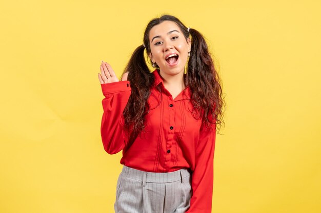 Vista frontal niña en blusa roja con expresión emocionada sobre fondo amarillo sentimiento femenino niño niña juventud emoción