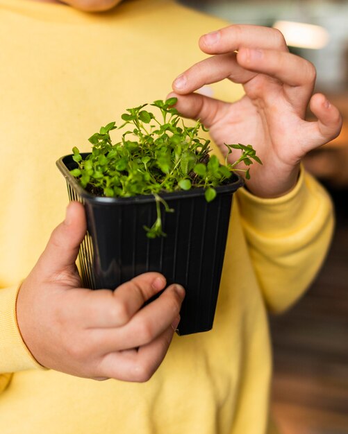 Vista frontal de la niña en casa con planta pequeña