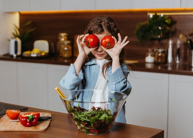 Vista frontal de la niña en la cocina con tomates