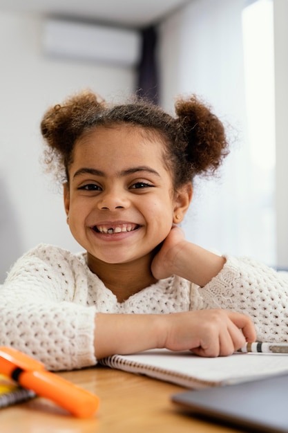 Vista frontal de la niña feliz en casa durante la escuela en línea con laptop