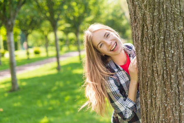 Vista frontal niña feliz posando detrás de un árbol