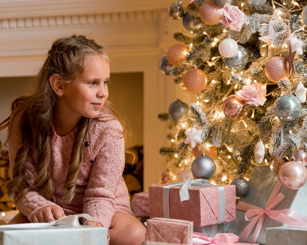 Vista frontal de la niña feliz con regalos y árbol de Navidad