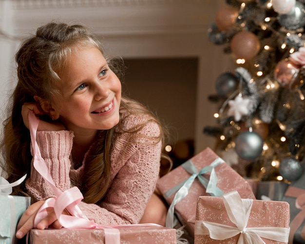 Vista frontal de la niña feliz con regalos y árbol de Navidad