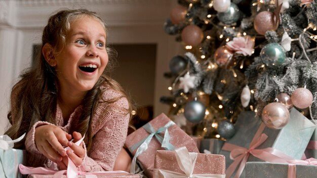Vista frontal de la niña feliz con regalos y árbol de Navidad