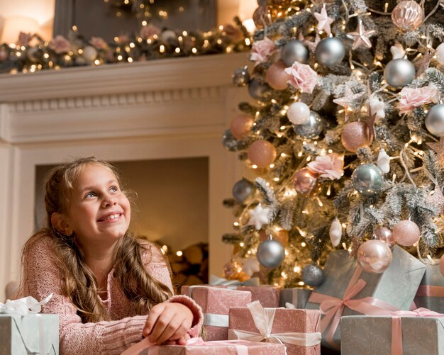 Vista frontal de la niña feliz con regalos y árbol de Navidad