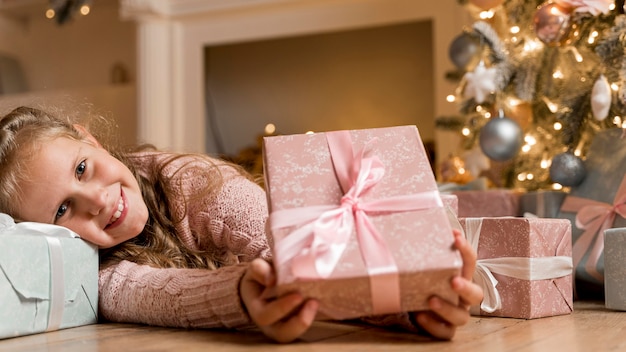 Vista frontal de la niña feliz con regalos y árbol de Navidad