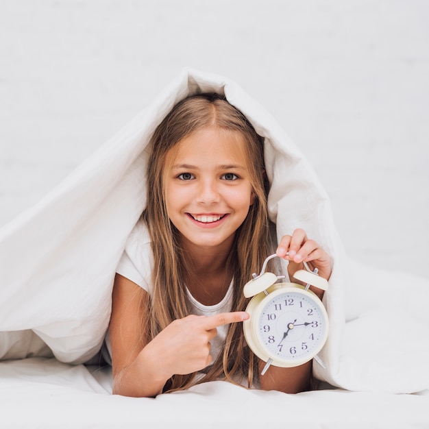 Vista frontal niña feliz señalando el reloj