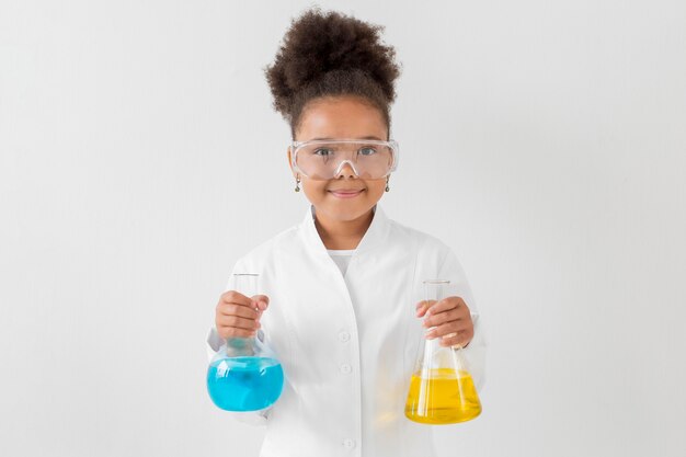 Vista frontal de la niña con gafas de seguridad y bata de laboratorio con tubos