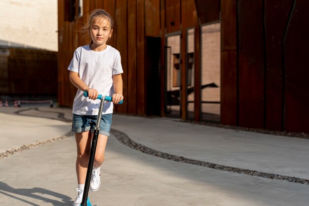 Vista frontal de la niña montando scooter azul