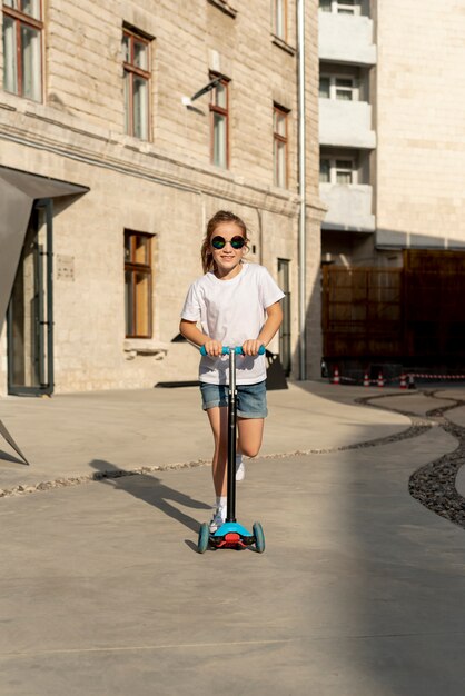 Vista frontal de la niña montando scooter azul