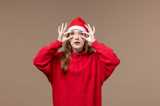 Vista frontal de la niña de Navidad abriendo los ojos sobre fondo marrón emoción de Navidad de vacaciones