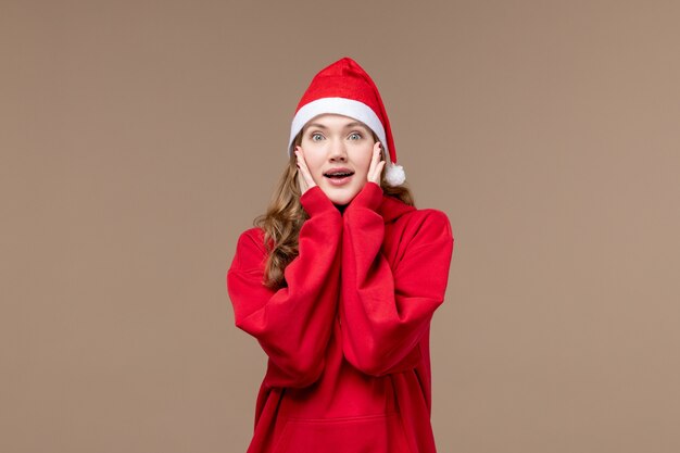 Vista frontal de la niña de Navidad con cara emocionada sobre fondo marrón modelo vacaciones Navidad