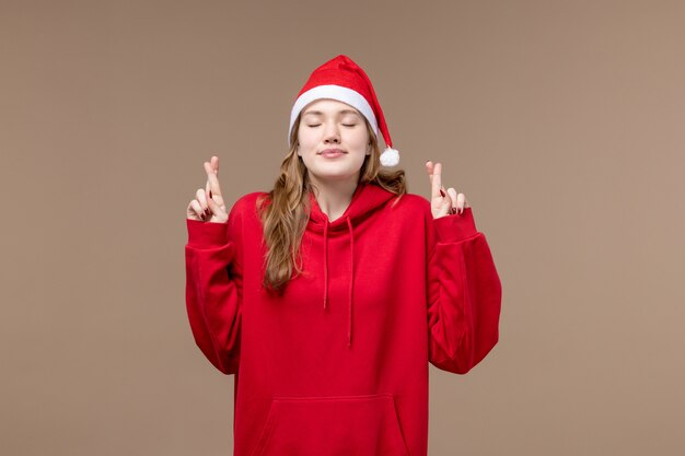 Vista frontal niña de navidad cruzando los dedos sobre fondo marrón modelo vacaciones navidad