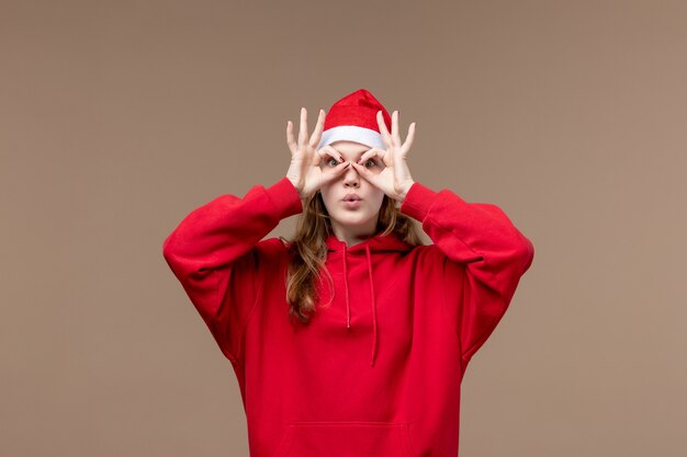 Vista frontal de la niña de Navidad mirando a través de sus ojos sobre fondo marrón emoción de Navidad de vacaciones