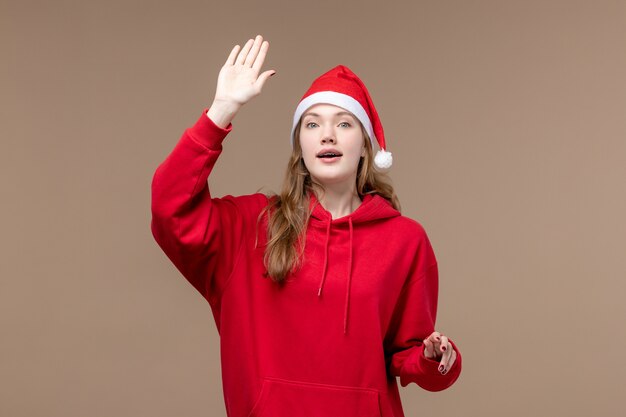 Vista frontal niña de navidad saludando sobre un fondo marrón mujer vacaciones navidad