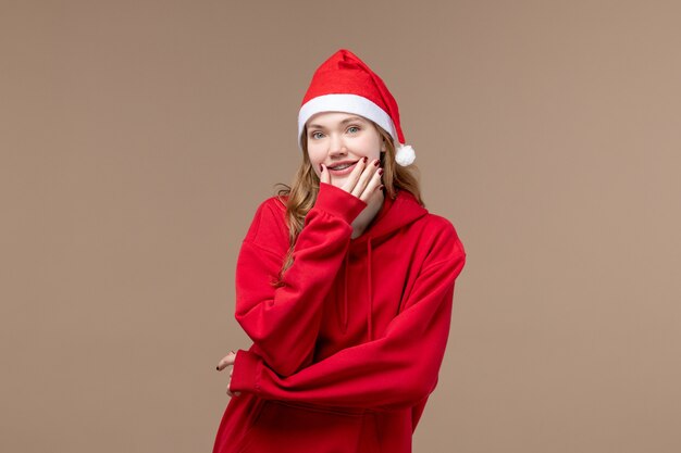 Vista frontal de la niña de Navidad tratando de sonreír sobre fondo marrón modelo vacaciones Navidad