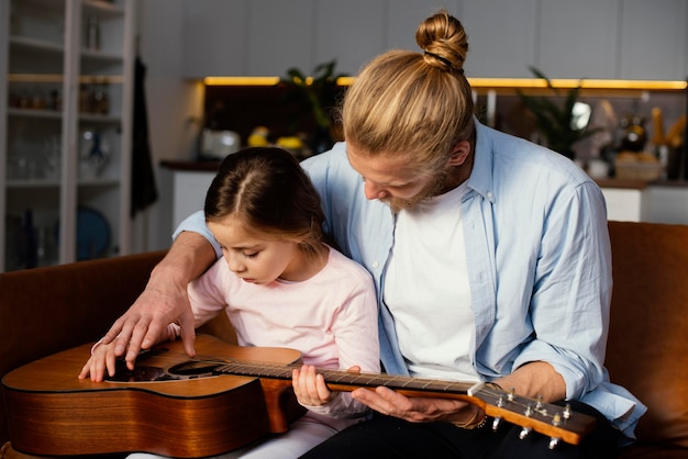 Vista frontal de la niña y el padre tocando la guitarra juntos